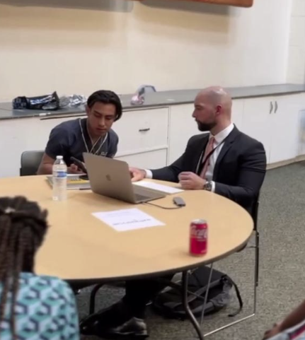 Joaquin Wilson teaching an asylum seeker how to use generative AI on a laptop for resume tailoring and job search.